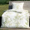 A duvet and pillow set with a botanical print is displayed on a wooden bench outdoors. Produktbild-Vorschau