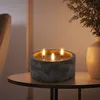 A three-wick LED candle in a concrete-look holder sits on a small round table next to a vase with greenery. Anteprima dell’immagine prodotto