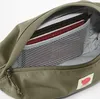 Close-up view of the inside of a green Fjällräven hip pack, showing books and a mesh pocket. Voir les images du produit