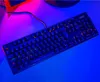 A black mechanical gaming keyboard with RGB lighting is placed on a surface with blue and pink lighting. Produktbild-Vorschau