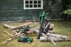 Gardening tools, including chainsaws and a leaf blower, are displayed on the grass in front of a wooden shed. Produktbild-Vorschau