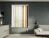 A display of vertical blinds in various colors, set against a dark gray wall with a kitchen counter and cabinets on the left, and a sofa on the right. Produktbild-Vorschau