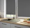 A kitchen sink area with dark gray pleated blinds on the window, a faucet, and some bread and fruit on the countertop. Produktbild-Vorschau