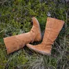 A pair of brown suede boots lying on the ground in grass and moss. Voir les images du produit