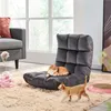 Two cats are playing on a fluffy rug in front of a window. One cat is sleeping on a floor chair, and another is walking on the rug. There are cat toys on the rug.