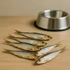 Several dried fish are arranged on a wooden surface next to a metal pet bowl. Produktbild-Vorschau