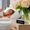 A woman is sleeping in bed next to a nightstand with a digital alarm clock and a vase of flowers. Anteprima dell’immagine prodotto