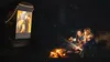 Two women sitting by a campfire at night, watching a movie projected from a vehicle. Náhled obrázku produktu