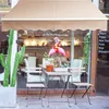 A storefront with a cafe setting outside, featuring plants and seating. Voir les images du produit