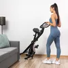 A woman in workout clothes stands next to a foldable exercise bike in a living room. Náhľad obrázku produktu