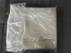 A folded beige fabric with white wavy trim, enclosed in clear plastic packaging, lying on a gray surface. Produktbild-Vorschau