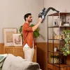 A man is using a cordless vacuum cleaner to clean the top shelf of a bookcase in a living room. Anteprima dell’immagine prodotto