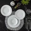 A table setting with white porcelain plates and bowls arranged on a black marble surface, accented by decorative elements like a candle holder and a succulent plant. Náhľad obrázku produktu