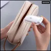 A person is holding a small white device with a clear case near an open beige pencil case. Náhľad obrázku produktu