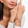 A close-up shot of a woman's wrist wearing a silver bracelet with red beads and charms. Produktbild-Vorschau