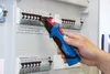 A hand holding a voltage tester near a circuit breaker panel. Náhľad obrázku produktu
