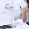 A phone charger plugged into a wall socket and connected to a phone on a table, with a person in the background holding a phone. Anteprima dell’immagine prodotto