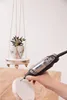 A person is using a Dremel rotary tool to drill into a round object, possibly for a DIY project. A small potted plant hangs in the background. Produktbild-Vorschau