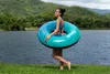 A woman is walking by a lake holding a large inflatable swim ring. Anteprima dell’immagine prodotto