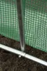 A close-up view of the base of a greenhouse structure, showing the metal frame and green netting. Náhľad obrázku produktu