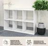 A white bookshelf with six compartments is shown next to a potted plant. There are also icons and text at the bottom of the image. Produktbild-Vorschau