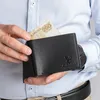 A person is holding a black wallet with a banknote sticking out. Anteprima dell’immagine prodotto