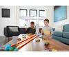 Two young boys are playing with a Hot Wheels track set on a wooden table in a living room. Produktbild-Vorschau