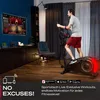 A man is exercising on a Sportstech crosstrainer in a living room, with a large TV screen displaying a workout program. Produktbild-Vorschau
