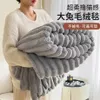 A person is holding a folded gray blanket in front of them, with a small table and perfume bottle in the background. Produktbild-Vorschau