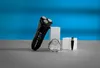 A black electric shaver and its accessories are displayed on a gray surface against a blue background. Voir les images du produit