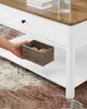 A hand places a woven basket onto the lower shelf of a white coffee table with a wood-grain top. Náhled obrázku produktu