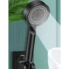 A black shower head with water spraying from it, set against a green striped background and a palm leaf. Produktbild-Vorschau