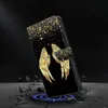 A black phone case with golden angel wings and glitter is displayed on a dark background with debris. Produktbild-Vorschau