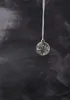 A clear glass ornament with LED lights inside, hanging from a white ribbon against a dark, textured background. Produktbild-Vorschau