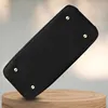 The bottom of a black handbag is shown resting on a wooden stand. Produktbild-Vorschau