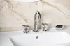 A close-up view of a modern chrome faucet with two handles and a soap dish with a bar of soap, set against a tiled wall. Podgląd zdjęcia produktu
