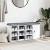 A white shoe bench with a gray cushion top, filled with various shoes, placed against a white wall with a mirror and a plant. Náhled obrázku produktu