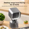 A small, modern-looking desktop range hood is placed on a kitchen counter next to some greenery and food. Produktbild-Vorschau