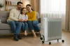 A family is sitting on a couch in a living room with a space heater in the foreground. Podgląd zdjęcia produktu