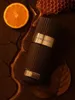 A perfume bottle is surrounded by natural elements like an orange slice, honeycomb, and leaves, suggesting a rich and natural fragrance. Voir les images du produit