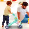 A toddler is playing with a walker in a bright, indoor setting, with an adult blurred in the background. Podgląd zdjęcia produktu