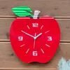 A red apple-shaped clock with a green leaf and brown stem, placed on a wooden surface. Produktbild-Vorschau