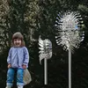 A young child sits on a rock in front of a hedge, with two kinetic wind sculptures to her right. Anteprima dell’immagine prodotto