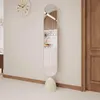 A full-length oval mirror with a beige base stands against a light-colored wall next to a wooden door. A clock is visible on the wall. Produktbild-Vorschau
