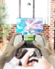 Hands holding a game controller with batteries inserted, in front of a TV screen. Produktbild-Vorschau