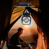 A person is sitting inside a tent at sunset, with a fan and light hanging above. Produktbild-Vorschau
