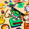 A close-up view of various Perler bead creations, with a green and black creature in the foreground being held by a string. Produktbild-Vorschau
