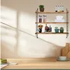 A three-tiered wooden shelf unit mounted on a wall, displaying various kitchen and decorative items. The foreground shows a wooden countertop with a slice of cake and a small bowl. Produktbild-Vorschau