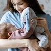 A woman is holding a baby and a stuffed bunny toy. Produktbild-Vorschau