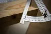A close-up shot of a wooden surface with a metal measuring tool, likely a protractor or angle finder, positioned on it. Produktbild-Vorschau
